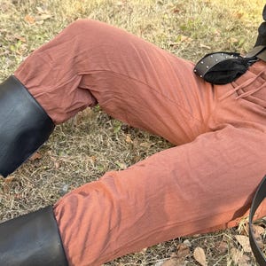 Puede incluir: Un pantal&oacute;n de lino marr&oacute;n con un cintur&oacute;n de cuero negro y una bolsa de cuero negro. El pantal&oacute;n lo lleva puesto una persona sentada en el suelo.