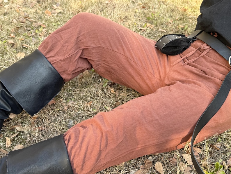 Puede incluir: Un pantal&oacute;n de lino marr&oacute;n con un cintur&oacute;n de cuero negro y una bolsa de cuero negro. El pantal&oacute;n lo lleva puesto una persona sentada en el suelo.