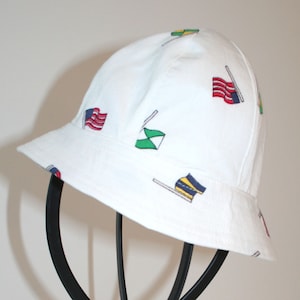 May include: White bucket hat with a pattern of colorful flags. The hat has a wide brim and a chin strap.