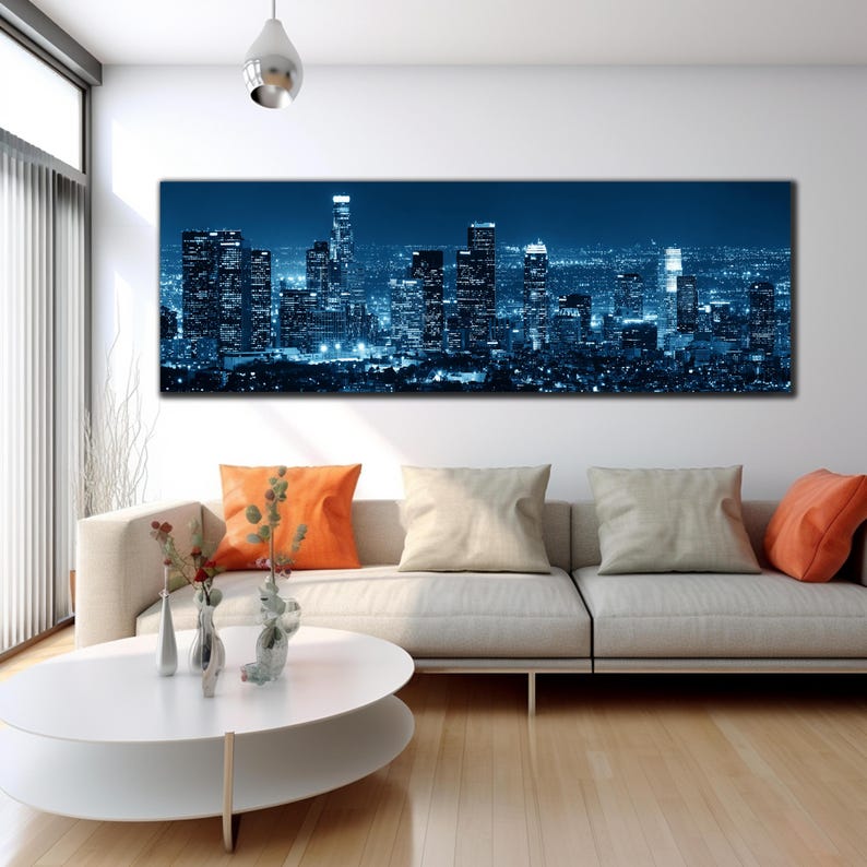 May include: A panoramic canvas print of a cityscape at night, dominated by tall, illuminated skyscrapers in shades of blue. The artwork hangs above a modern sofa with orange and beige throw pillows, creating a contemporary living room setting.