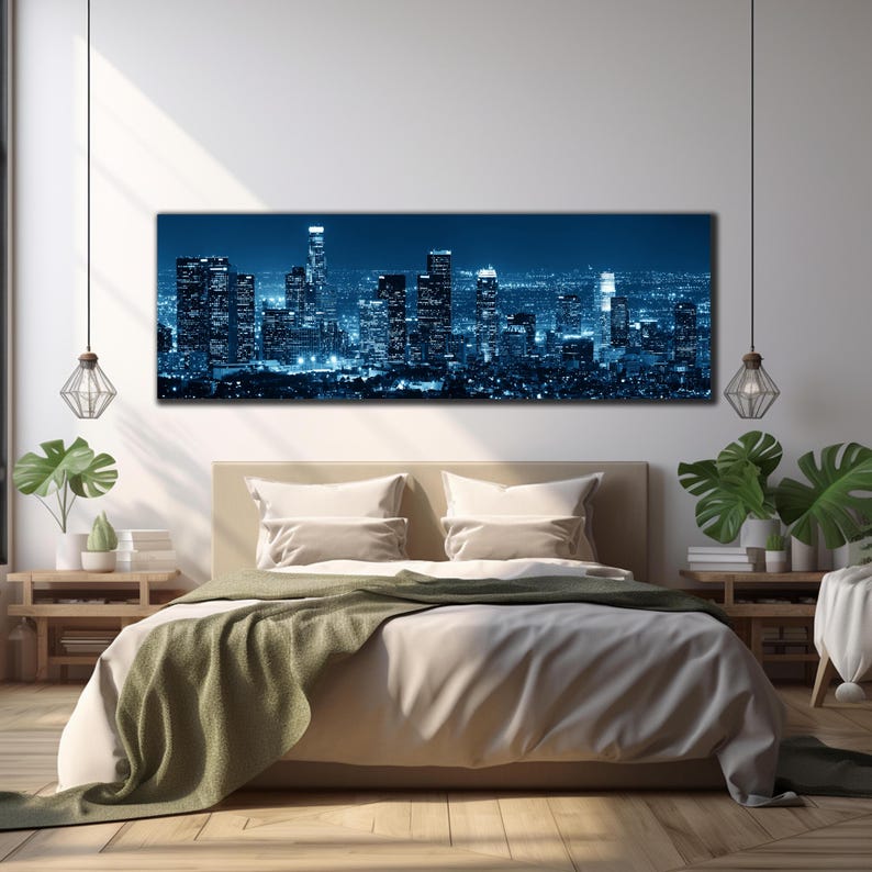 May include: A large rectangular canvas print of a cityscape at night, dominated by tall buildings illuminated in shades of blue. The print hangs above a bed with beige bedding and a green throw. The room is decorated with plants and pendant lights.