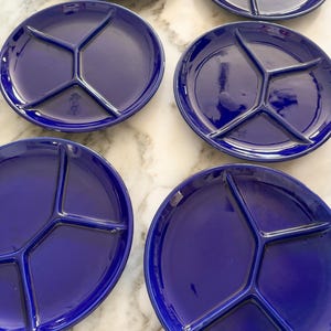 May include: A set of six circular, deep blue ceramic plates, each featuring a Y-shaped divider that creates three distinct sections. The plates have a smooth, glossy finish and are arranged in a grid pattern on a light-colored surface.