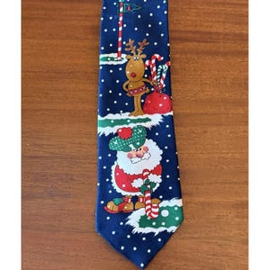 May include: Navy blue Christmas-themed necktie featuring a repeating pattern of white snowflakes. The tie showcases Santa Claus, a reindeer, and candy canes on a snowy green landscape. The tie is a festive accessory.