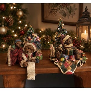 May include: Two decorative resin figurines featuring brown teddy bears with Christmas themes. One bear holds a scroll and wears a red blanket, while the other wears a Santa hat and sits beside a decorated Christmas tree with wrapped gift boxes.