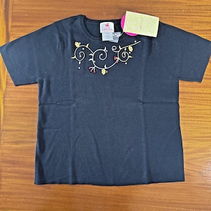 May include: Black short-sleeved t-shirt with a crew neck. The shirt features an embroidered design of gold-colored vines and red berries across the chest. A tag is attached to the shirt.