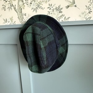 May include: A bucket hat featuring a dark green and navy blue plaid pattern. The hat has a rounded crown and a downward-sloping brim, constructed from a textured fabric that displays a visible weave throughout the entire surface of the headwear.
