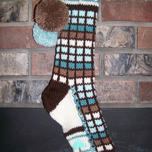 Puede incluir: Una media de punto marrón y azul con un puño blanco y un pompón marrón en la parte superior.