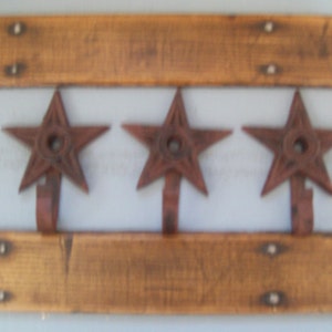 May include: Three rustic star-shaped hooks mounted on a wooden board. The hooks are made of metal and have a rusty brown finish. The board is made of wood and has a natural brown finish.
