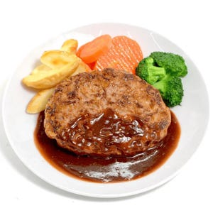 May include: A plate of food featuring a large, round hamburger steak covered in a rich brown gravy. The plate also includes golden potato wedges, sliced carrots, and green broccoli florets. The food is arranged on a white plate.
