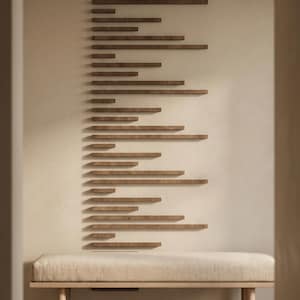 May include: A modern interior scene featuring a series of wooden shelves arranged in a linear pattern on a light-colored wall. Below, a bench with a neutral-toned cushion and wooden frame provides seating. The design creates a minimalist, contemporary aesthetic.