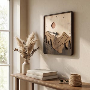 May include: A square wooden wall clock with a mountain scene. The clock features a dark brown frame, a light brown background, and a mountain range design. The clock hands are black. The clock is mounted on a beige wall.