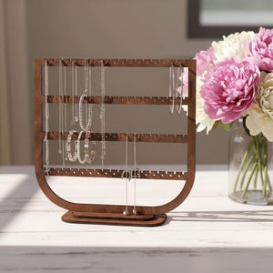 May include: A wooden jewelry organizer with multiple rows of holes for hanging necklaces, bracelets, and earrings. The organizer is a dark brown color and has a curved base. Several pieces of jewelry are displayed on the organizer.