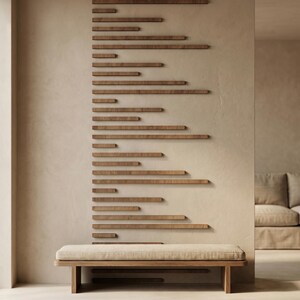 May include: A modern interior scene featuring a wooden bench with a beige cushion. Above the bench, a series of horizontal wooden planks are mounted on a beige wall. The planks vary in length and create a unique design element. A sofa is visible in the background.