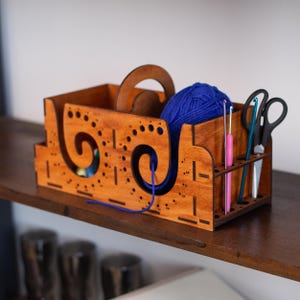 May include: Wooden yarn organizer with a blue ball of yarn, a wooden yarn winder, and a set of crochet hooks and scissors.