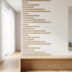 May include: A modern interior featuring a light wood bench and a white wall adorned with horizontal wooden slats of varying lengths. The room has hardwood flooring and a sheer white curtain, creating a minimalist aesthetic.