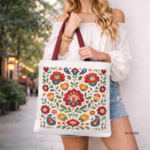 May include: A white tote bag with dark red straps featuring a symmetrical floral pattern in shades of red, yellow, blue, and green. The design includes stylized flowers, leaves, and paisley shapes arranged in a balanced, decorative composition.