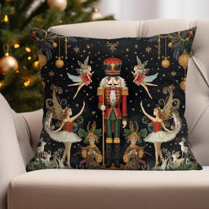 May include: Decorative throw pillow with a black background featuring a Nutcracker soldier in a red and green uniform, surrounded by fairies and deer. The pillow has gold accents and is decorated with Christmas ornaments.