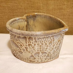 May include: A heart-shaped ceramic bowl with a white glaze and a textured, lace-like design. The bowl is made by hand and has a rustic, farmhouse style.