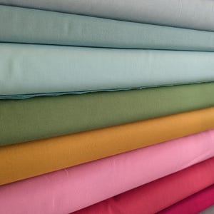 May include: A stack of fabric rolls in various colors, including shades of blue, green, yellow, pink, and red. The fabric appears to be a solid color cotton or linen, with a smooth texture. The rolls are neatly stacked, showcasing the range of hues.