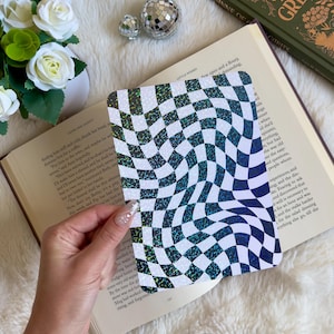 May include: A holographic sticker with a black and white checkered pattern that appears to be swirling. The sticker has a glittery finish.
