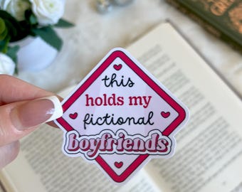 May include: A pink and white diamond-shaped sticker with the text "this holds my fictional boyfriends" in black and white. The sticker has small pink hearts around the edges.