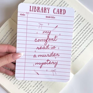 Puede incluir: Una tarjeta de biblioteca blanca con un diseño de papel rayado y las palabras "LIBRARY CARD" en la parte superior. La tarjeta presenta el texto "my comfort read is a murder mystery" en un estilo manuscrito, junto con ilustraciones decorativas de lazo y cuchillo.