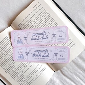 May include: Two pink and white bookmark stickers with the text "coquette book club - read a book on everything I say" and a cute illustration of a bunny reading a book. The stickers have a ticket-like design with a small cherry graphic.
