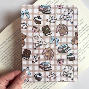 Può includere: Un foglio di adesivi decorativo con un motivo ripetuto di illustrazioni accoglienti. Il foglio presenta disegni di libri, caffettiere, maglioni, calzini, tazze, fiocchi e animali di peluche in morbidi colori pastello.