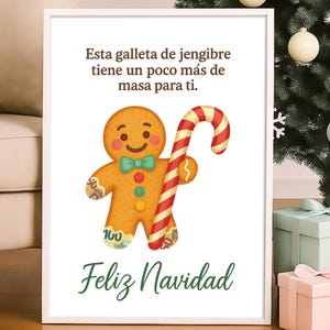 May include: A framed print featuring a gingerbread man holding a candy cane. The gingerbread man has a green bow tie and is decorated with frosting. The text "Esta galleta de jengibre tiene un poco más de masa para ti. Feliz Navidad" is written on the print.
