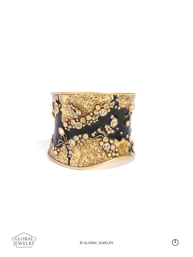 May include: A wide, gold-toned cuff bracelet with a textured, black and gold design. The bracelet is embellished with numerous clear, round gemstones. The words "GLOBAL JEWELRY" are printed on the bottom left.