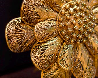 May include: Close-up of a gold-colored, filigree flower. The flower has detailed, openwork petals and a textured center. The intricate design and warm metallic hue create a luxurious aesthetic. The flower is likely a decorative element.