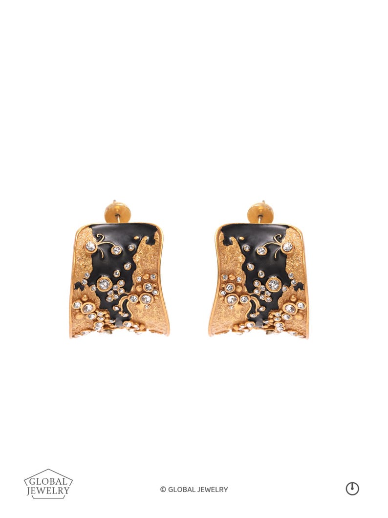May include: A pair of gold-toned earrings with a black enamel design and sparkling clear gemstones. The earrings have a rectangular shape with a curved edge and a post backing. The design includes floral and abstract elements.