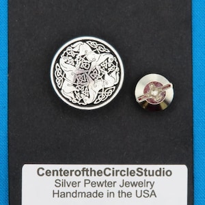 May include: A silver pewter jewellery set featuring a round button with a Celtic knot design and a smaller pin. The jewellery is displayed on a black card with the text "Center of the Circle Studio, Silver Pewter Jewelry, Handmade in the USA."