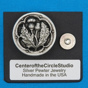 May include: A silver pewter thistle flower pendant on a black background. The pendant is displayed on a card that reads "CenteroftheCircleStudio Silver Pewter Jewelry Handmade in the USA".