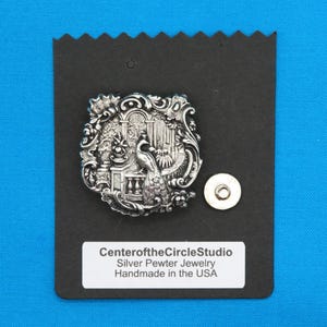 May include: Silver pewter jewelry pendant featuring a detailed design of a peacock in a garden setting. The pendant is on a black background with a label that reads "CenteroftheCircleStudio Silver Pewter Jewelry Handmade in the USA".