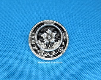 May include: A silver button with a black enamel center featuring a raised silver flower design.