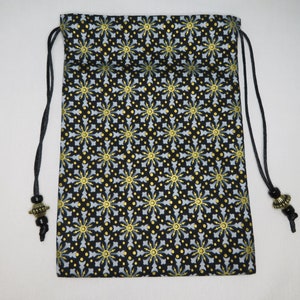 May include: A black drawstring bag with a gold and white geometric pattern. The bag has black drawstrings with gold beads at the ends.