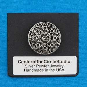 May include: A silver pewter jewelry button with a circular design featuring a starburst pattern. The button is on a black background with a white label that reads "CenteroftheCircleStudio Silver Pewter Jewelry Handmade in the USA".