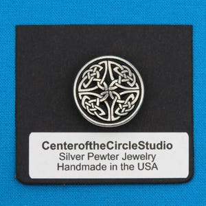 May include: A silver pewter Celtic knot pendant on a black background. The pendant is round and features a detailed knot design. The text "CenteroftheCircleStudio Silver Pewter Jewelry Handmade in the USA" is printed on a white label below the pendant.