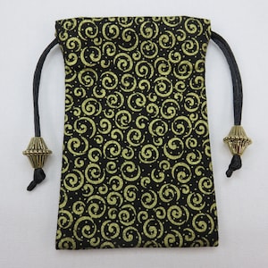 May include: A black drawstring bag with gold glitter swirls and a gold metal toggle. The bag is made of fabric and has a black drawstring.