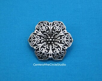 May include: A silver-toned metal flower-shaped button with intricate scrollwork design.