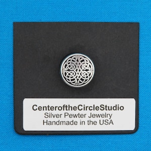May include: A silver pewter Celtic knot pendant on a black background. The pendant is round and features a detailed knot design. The text "CenteroftheCircleStudio Silver Pewter Jewelry Handmade in the USA" is printed on a white label below the pendant.