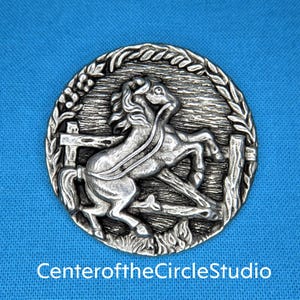 May include: A silver-toned metal button featuring a detailed design of a horse leaping over a fence. The button is circular and has a textured surface.
