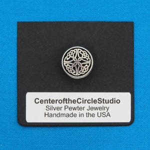 May include: A silver pewter button with a Celtic knot design, set on a black card. The button is round with an intricate pattern. The card has a white label with the text "Center of the Circle Studio, Silver Pewter Jewelry, Handmade in the USA."