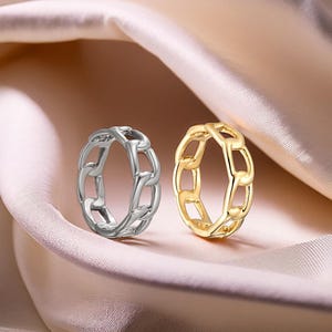 May include: Two chain link rings, one silver and one gold, on a pink fabric background.