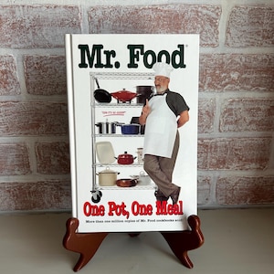 May include: A green and white cookbook titled "Mr. Food One Pot, One Meal" with a picture of a man in a white chef's hat and apron standing next to a metal shelving unit with pots and pans on it. The text "More than one million copies of Mr. Food cookbooks sold!" is printed below the title.