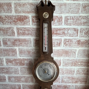 May include: A vintage wooden weather station with a thermometer, barometer, and small dial. The thermometer shows a temperature reading in Fahrenheit. The barometer dial indicates weather conditions. The wooden frame is a dark brown color.