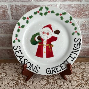 May include: A white ceramic mug with a black handle and the text "But First, Coffee" in a bold, black font. The mug is set against a blurred background, suggesting a cozy setting.