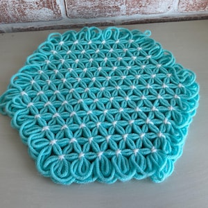 May include: A turquoise crocheted doily with a white center. The doily is made of yarn and has a scalloped edge.