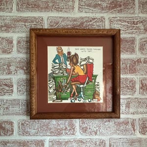 May include: Framed vintage cartoon print featuring a woman at a desk overwhelmed by paperwork, with a man in the background. The text reads "AND WHEN YOU'RE THROUGH WITH THAT..." The frame is a dark wood color.